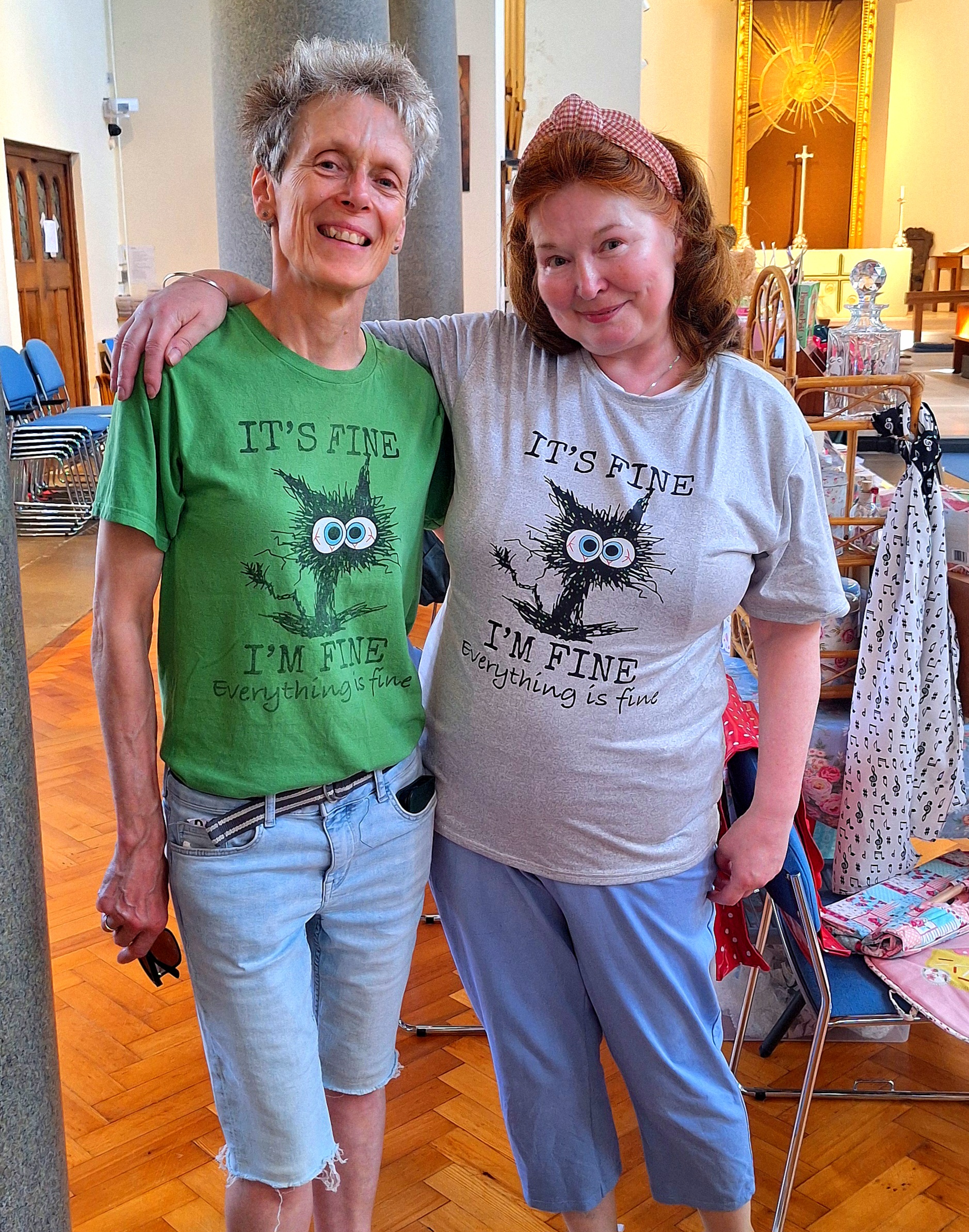 Two women in matching T-shirts stand smiling side-by-side, with their arms around each other