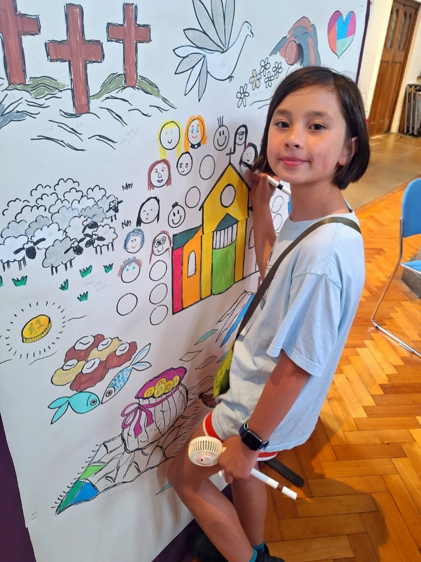 A child stands smiling as she colours a large, illustrated canvas